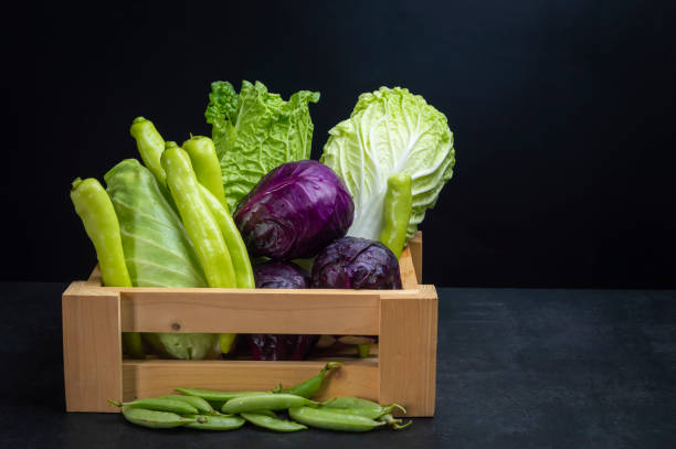 Fresh green and purple vegetables with vitamins in wooden crate on black background.
