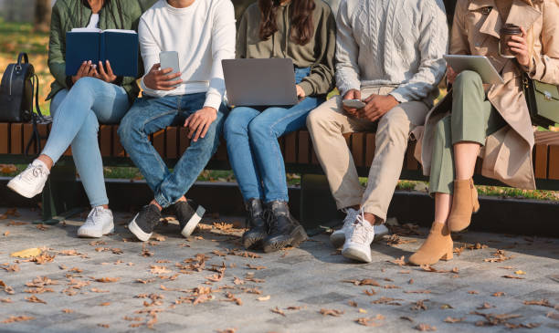 istock Group of students sitting on bench in park and studying 2179167185