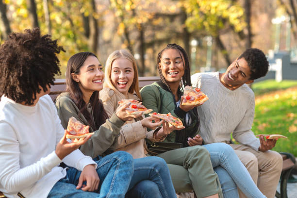 istock Positive friends sitting on bench at park, eating pizza 2179167281