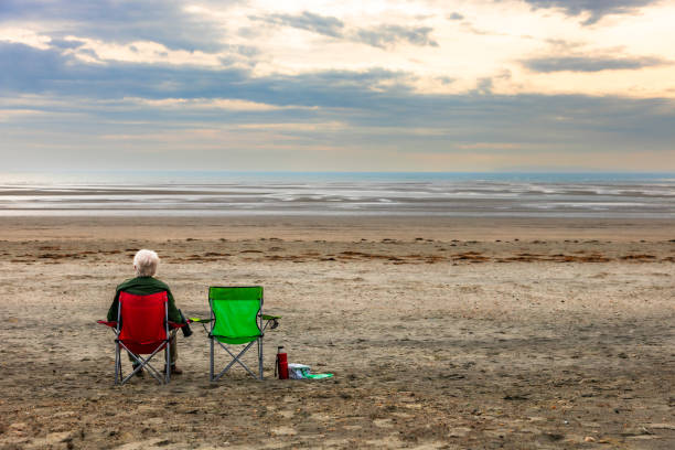 istock Lonely senior man sitting on chair on empty beach at sunset 2179167748
