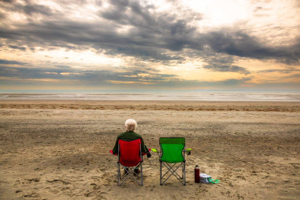 istock Lonely senior man sitting on chair on empty beach at sunset 2179167756