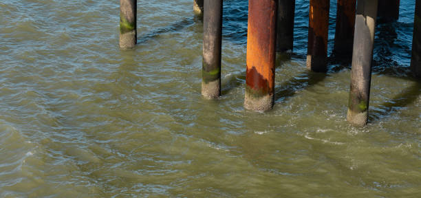 Rusty and weathered pillars of a pier. Waves breaking between the pillars. Calm North Sea, shallow waves, sunny day, beach in The Hague, Netherlands.