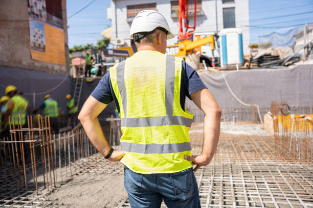 istock Worker in safety vest and helmet, standing on construction site, focused on work flow 2179170244