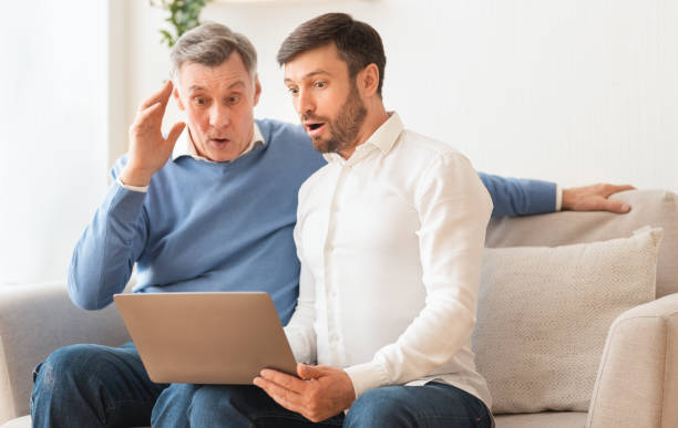 istock Shocked elderly man and adult son using laptop sitting indoor 2179170873