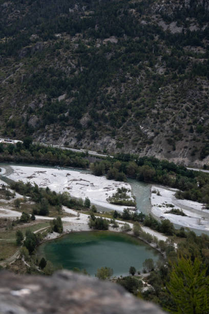 Aerial view of a winding river passing through a mountainous valley with a nearby green lake and lush vegetation, creating a unique natural landscape.