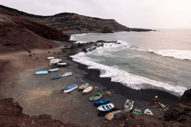 fishing boats on the volcanic beach of Ciclos against foamy ocean in Yaiza, Lanzarote at Canary Islands, Spain, concept of wild nature and marine lifestyle