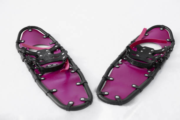 young sportsman walks in crimson snowshoes and leggings on snow, close-up view of legs, winter hiking concept, active lifestyle