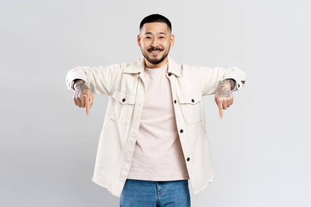 istock Smiling asian man with tattoos pointing down with both hands on a white background 2179185731