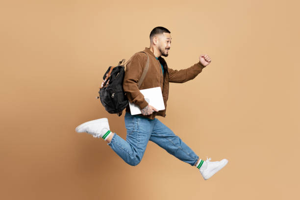 istock Young student running and jumping with laptop and backpack 2179186131