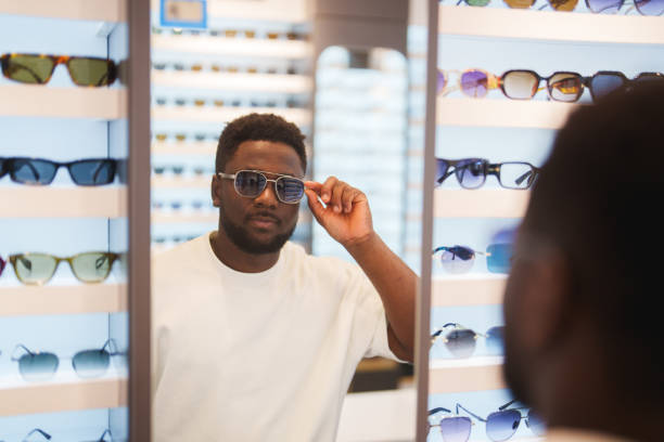 istock Young man trying on sunglasses in optic store, looking at mirror. 2179186203