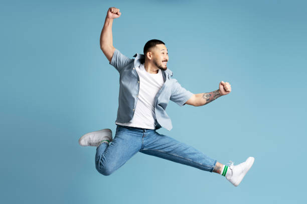 istock Young man jumping showing positive emotions on blue background 2179187481