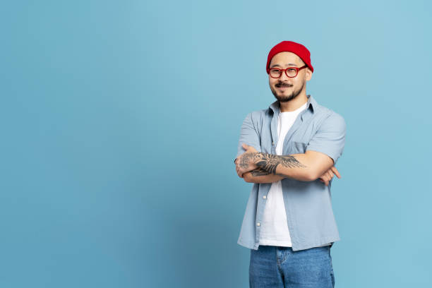 istock Confident creative man smiling with folded arms and tattoos on blue background 2179187856