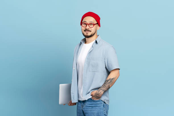 istock Asian man holding laptop and smiling on blue background 2179188037