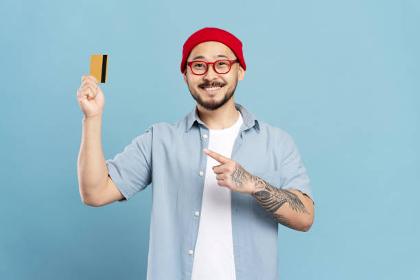istock Smiling man showing credit card and pointing at it on blue background 2179188233