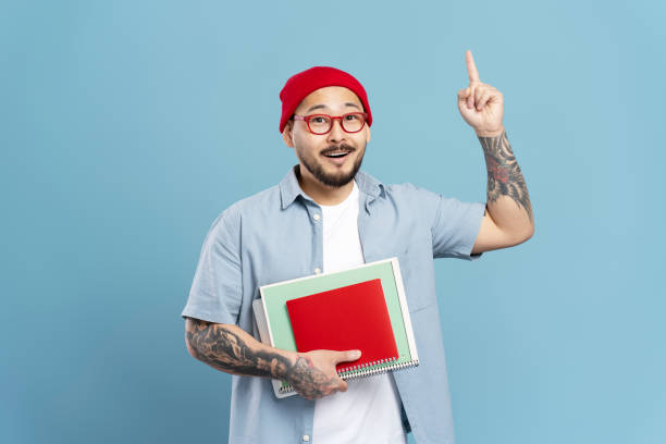istock Asian man having an idea is holding notebooks and pointing upwards 2179188531
