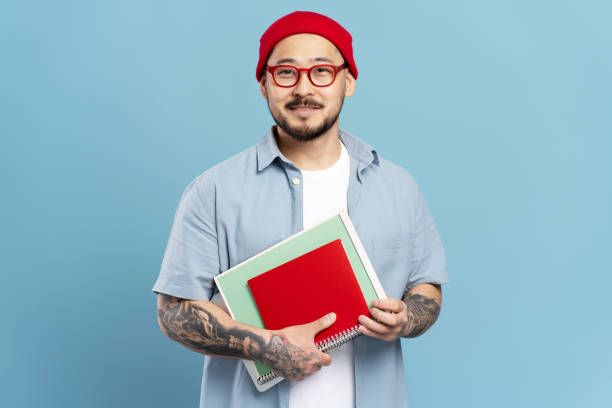 Asian male student holding notebooks on blue background