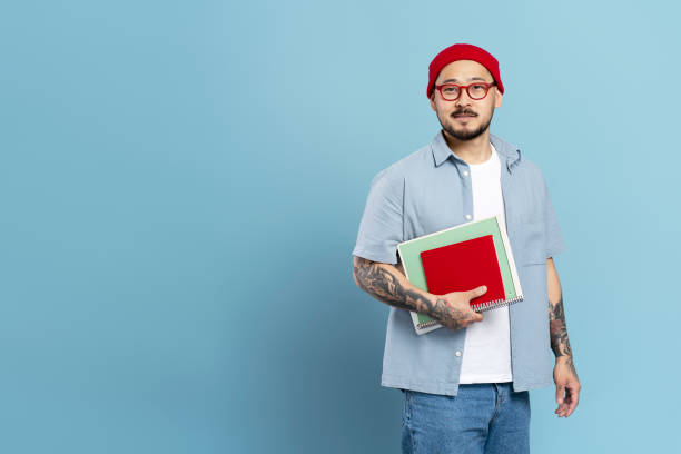 istock Confident tattooed student holding books on blue background 2179188646