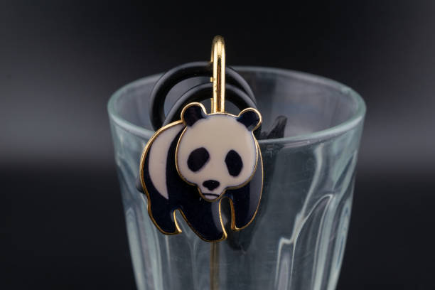 A cute panda-themed hair tie attached to a gold loop, placed on the rim of a glass cup. The black and white panda design adds a playful touch to this everyday hair accessory.