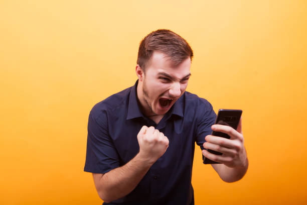 istock Young man screaming at the smartphone on yellow background 2179201045