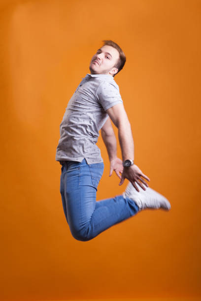 A young woman with a shaved head jumps in the air with happy emotion.  The sky behind her is vibrant blue.