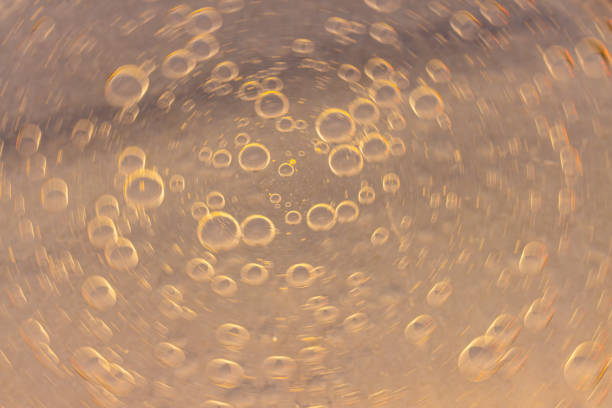 This macro photograph features an abstract background with circular shapes resembling droplets. The warm gradient of colors ranging from yellow to orange creates an interesting visual effect with the translucent circles. The varying sizes and overlapping of the circles add depth and texture, making this image perfect for artistic and creative projects.