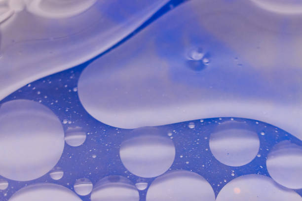 This macro photograph features an abstract background with a blue hue, adorned with water droplets of various sizes. The droplets are scattered across the surface, some forming smaller clusters while others stand alone. The light reflection and color distortion created by the droplets add depth and texture to the image, making it ideal for artistic and creative projects.