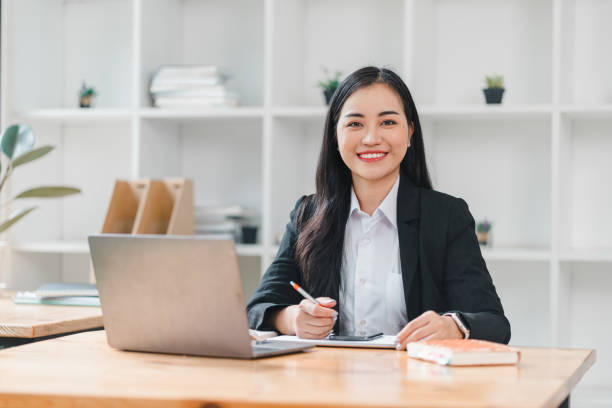 istock confident businesswoman smiles while working at her desk, showcasing modern office environment. She is engaged with her laptop and notes, reflecting professionalism and productivity. 2179218869
