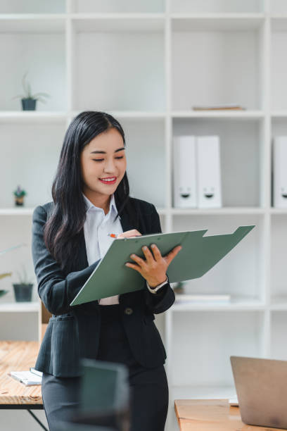 istock professional woman in black suit is smiling while holding clipboard and taking notes in modern office setting. Her confident demeanor reflects positive work environment. 2179219022