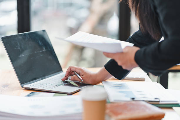 istock person is working on laptop while holding documents, surrounded by office materials, conveying sense of productivity and focus. 2179219323
