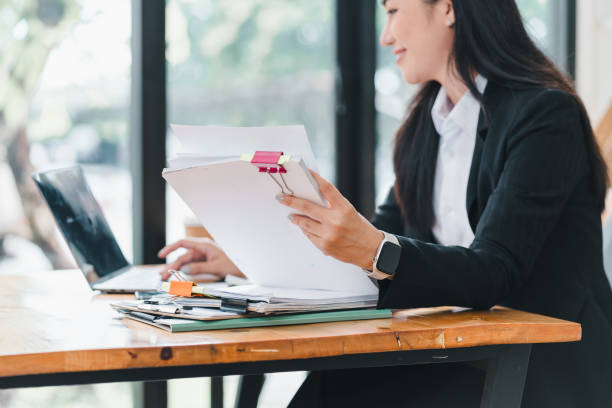 istock professional woman is working at desk, reviewing documents while using laptop. scene conveys sense of productivity and focus in modern office environment. 2179219359