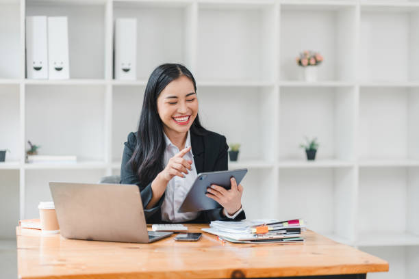istock young woman in black suit smiles while using tablet at her desk, surrounded by office supplies and laptop. Her cheerful demeanor reflects productive work environment. 2179219384