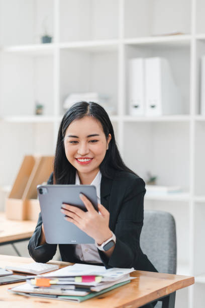 istock young woman in black suit smiles while using tablet in modern office setting, surrounded by organized paperwork and clean workspace. Her expression conveys happiness and engagement. 2179219390