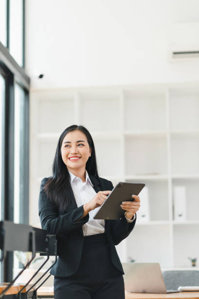 istock professional woman in black suit smiles while holding tablet in modern office setting. bright, airy space features large windows and minimalist decor, creating inviting atmosphere. 2179219483