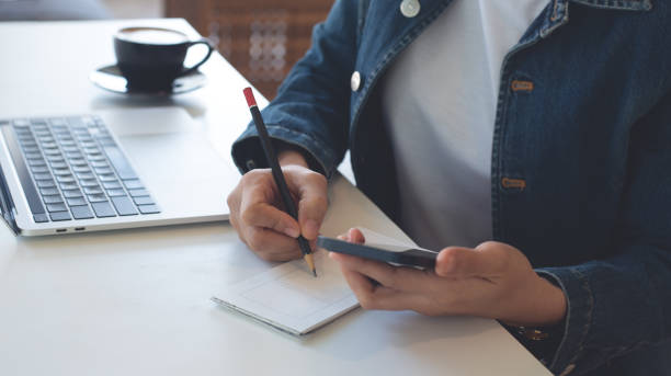 istock Young asian business woman working on laptop computer and writing on notepad on table at coffee shop. Smiling freelancer online working, planning new project, freelance at work 2179222016
