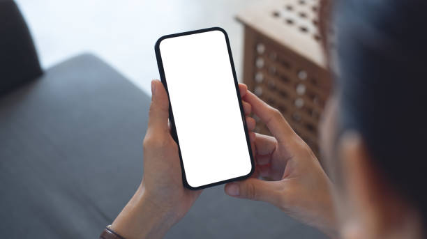 istock Cell phone white blank screen mockup, woman's hand holding mobile phone with blank screen and a cup of coffee in coffee shop, over shoulder view 2179222042