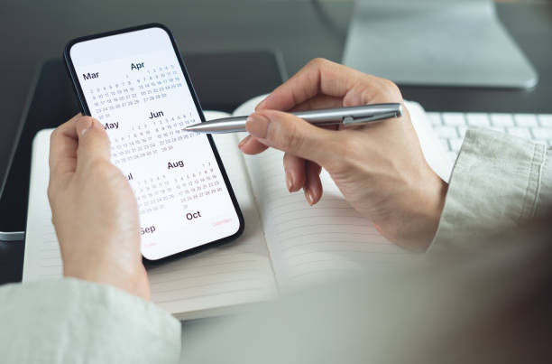 istock 2025 Calendar event planner timetable agenda plan on organize schedule. Business woman using mobile phone with monthly calendar for event planning, Plan scheduling with laptop on office table 2179222084