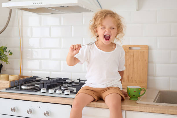 istock Overjoyed toddler enjoying delicious meal while sitting kitchen counter smiling with widely open mouth while eating her favorite food during lunchtime at home 2179223302