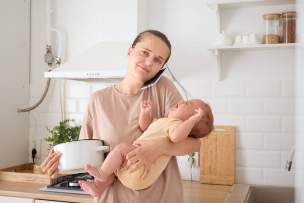 istock Mom multitasking cooking for her infant child and having conversation on smartphone talking on mobile phone while preparing food in kitchen 2179223321
