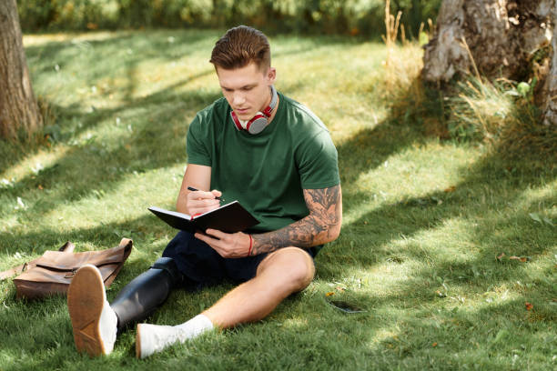 A young man with an artificial limb enjoys creative writing in a serene outdoor setting