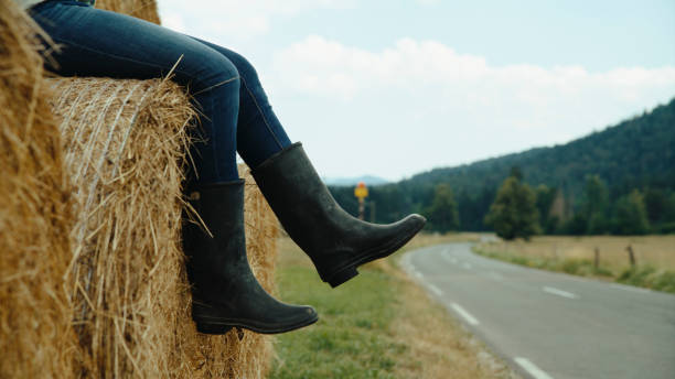 Man in boots walks on newly laid straw covering after sowing grass agricultural field.