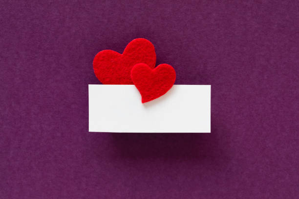Red heart shapes attached to a blank white greeting card on purple background.