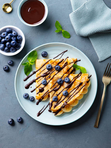 istock Crepes, thin pancakes with chocolate sauce and fresh blueberries. Grey background. Top view. 2179325214