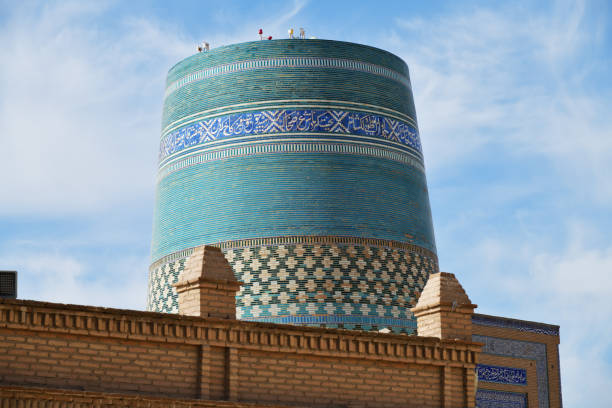 Khiva, Uzbekistan - Sept 15, 2024: Ancient architecture and Kalta Minor minaret at Muhammad Amin Khan Madrassah. Large blue minaret decorated with ornamented belts of glazed tile
