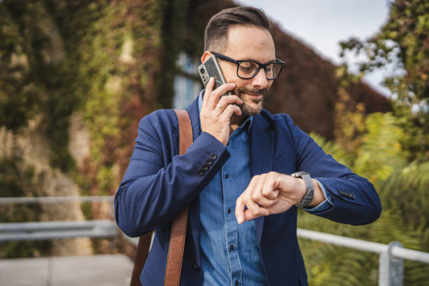 istock Businessman talk on mobile phone and check time on wrist watch 2179431743
