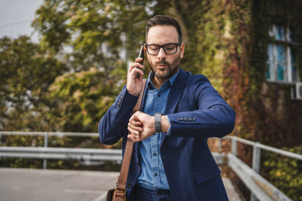 istock Wistful businessman talk on mobile phone and check time on wrist watch 2179431792