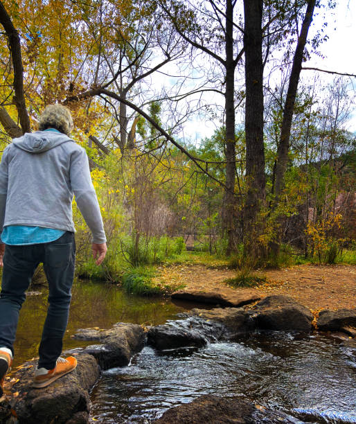 Santa Fe, NM: A senior man crossing the Santa Fe River on a series of rocks in autumn.