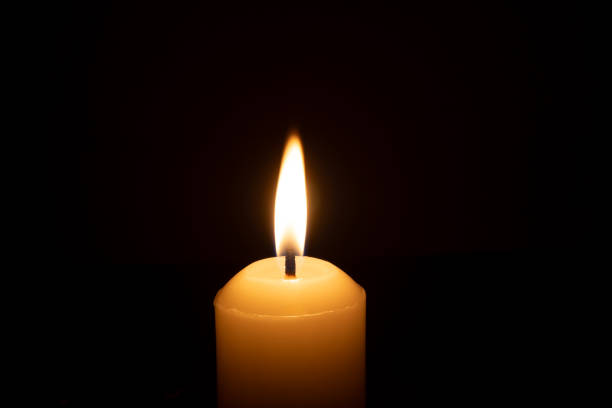 istock A single burning candle flame or light glowing on a big white candle isolated on red or dark background on table in church for Christmas, funeral or memorial service 2179493295