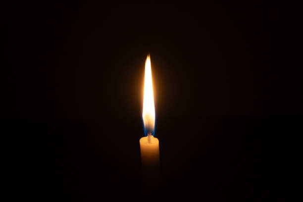 istock A single burning candle flame or light glowing on a small orange candle on black or dark background on table in church for Christmas, funeral or memorial service with copy space 2179493438