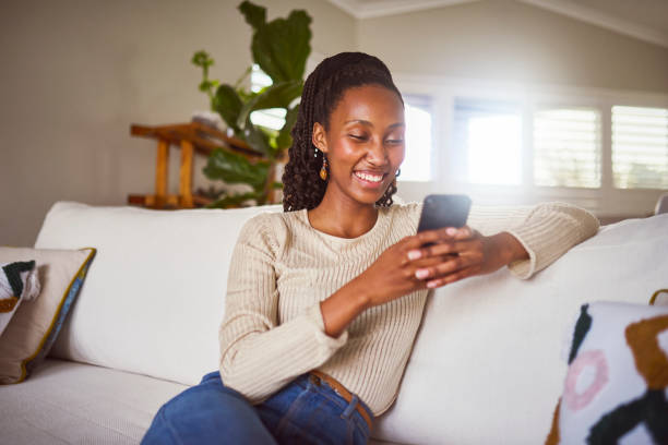 istock Cheerful young woman using cellphone on sofa at home 2179497314