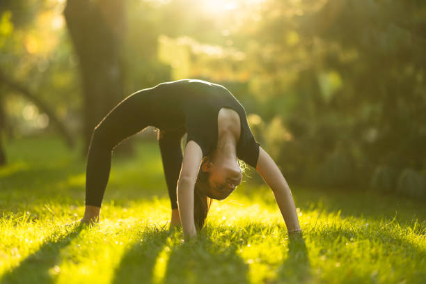 Full length shot of girl in black leotard doing bridge exercise in nature at sunset